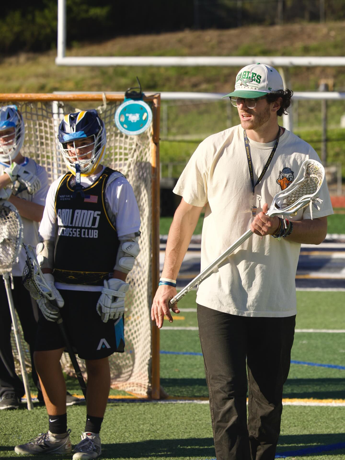 Aidan Niklaus walking past players with stick at Kooks Lacrosse Club clinic
